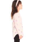 Side view of young girl wearing Chaser’s light pink Allover Pink Skiers long sleeve top with skier patterns on a white background
