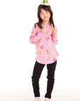 Full body view of girl wearing Chaser’s pink Tossed Candy Canes Long Sleeve with colorful candy cane designs, a Christmas tree hat, and black pants on a white background