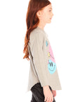 Side view of girl wearing Chaser’s Heather Grey Colorful Smileys long sleeve pullover with colorful smiley face designs and black jeans on a white background