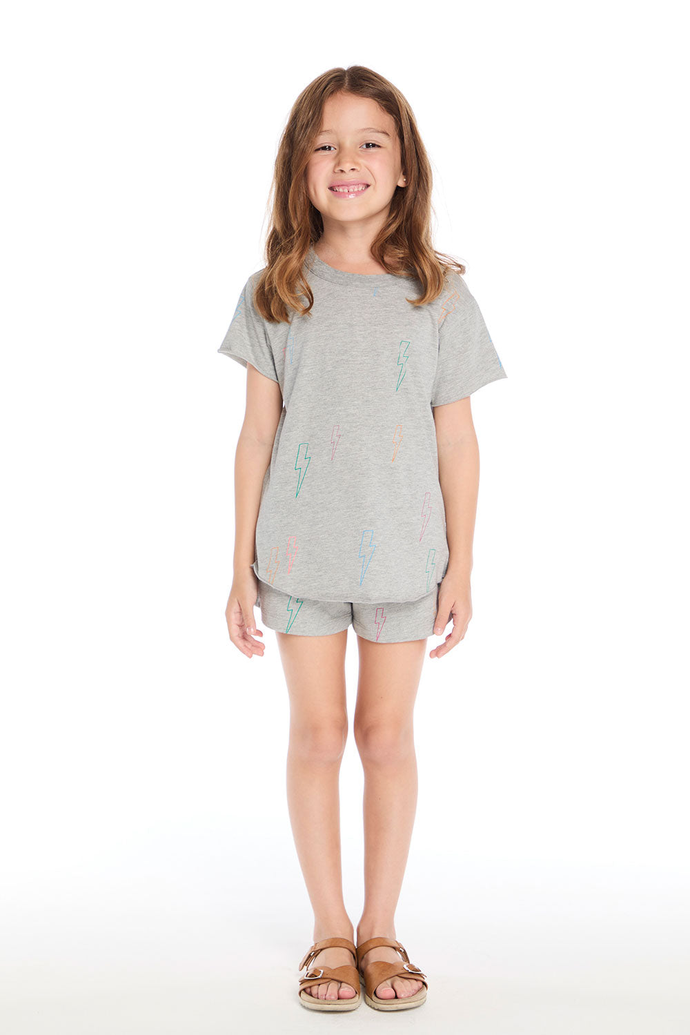 Girl wearing the Chaser Kids Neon Bolts Shorts paired with the matching Neon Bolts Shirttail Tee, styled with sandals on a white background