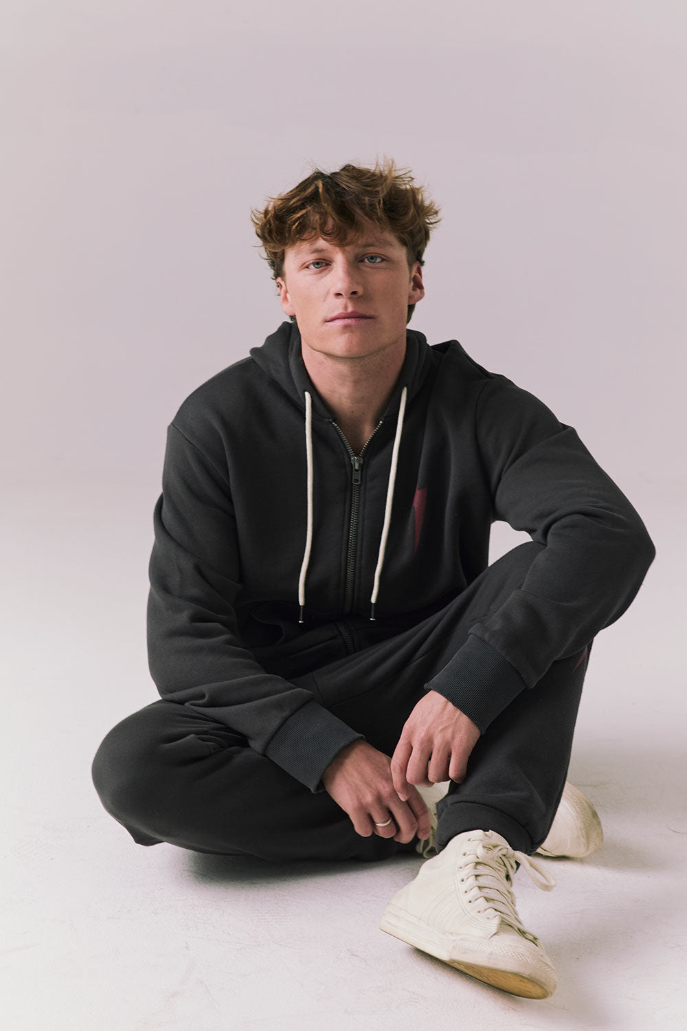 Full body view of model sitting wearing Bolt Black Hoodie with matching pants.