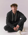 Full body view of model sitting wearing Bolt Black Hoodie with matching pants.
