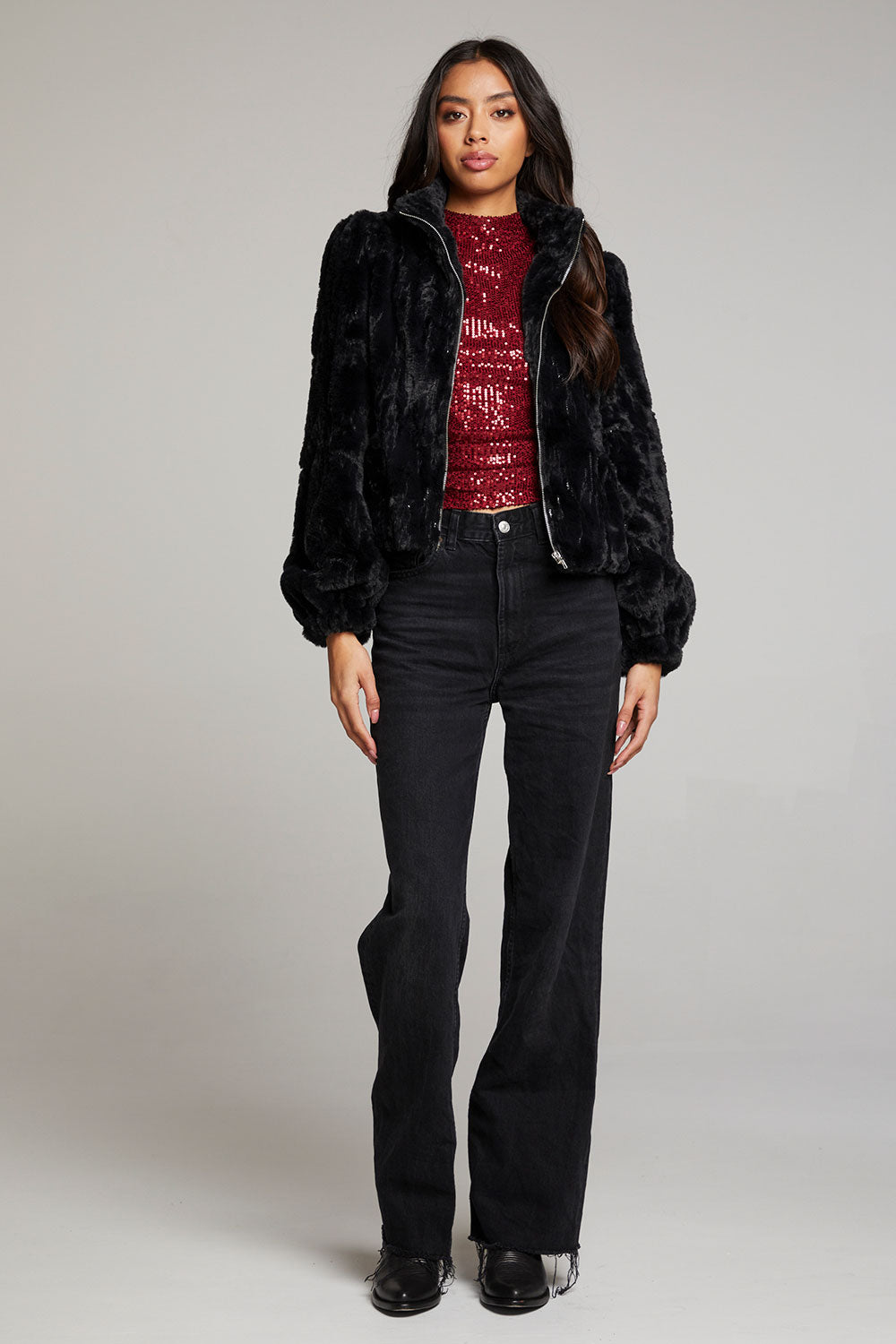 Full body view of woman wearing Chaser’s Puff Sleeve Licorice Jacket styled with a red sequin top and black pants on a plain background
