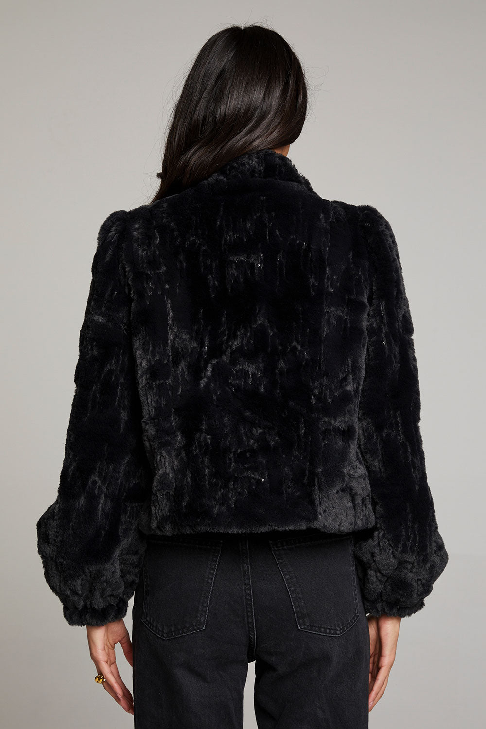 Back view of woman wearing Chaser’s Puff Sleeve Licorice Jacket showing shoulder detail on a plain background