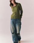 Full front view of model wearing the Varsity Star Sweater in bronze green with slouchy fit and twin arm stripes and blue jeans on a plain background