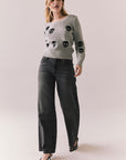 Woman wearing the Tossed Skulls Long Sleeve sweater in Heather Grey with allover black skull motif and fitted silhouette standing against a plain background.
