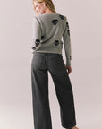 Back view of a woman wearing the Tossed Skulls Long Sleeve sweater in Heather Grey with allover black skull motif and fitted silhouette standing against a plain background.
