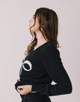 Side view of woman wearing Chaser’s true black Bow Long Sleeve with a visible white bow design on a plain background.