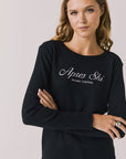 Woman wearing Chaser's black Apres Ski Milano Military Thermal Long Sleeve Tee with 'Apres Ski' text on a plain background