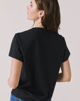 Back view of woman wearing Chaser’s black Tini Time Tee on a plain background