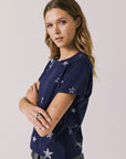 Side view of woman wearing Chaser's Allover Distressed Stars Tee with star patterns on a plain background