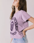 Side view of woman wearing Chaser’s The Rolling Stones ’78 Tour Amethyst Purple Tee on a plain background