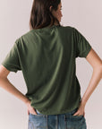 Back view of model wearing Woodstock Festival Flower Tee in bronze green against a plain background
