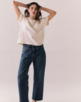 Woman standing against a plain background wearing the Rambler Starry White Tee with ringer neck and cap sleeves and blue jeans