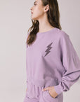 Side view of woman wearing Chaser’s Bolt Amethyst Purple Pullover with matching joggers on a plain background