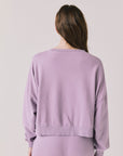 Back view of woman wearing Chaser’s Bolt Amethyst Purple Pullover with matching joggers on a plain background