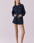 Full body view of woman wearing Chaser’s navy Tossed Bows Long Sleeve with matching Tossed Bow shorts featuring small bow prints on a white background