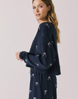 Side view of woman wearing Chaser’s navy Tossed Bows Long Sleeve with bow pattern on a white background