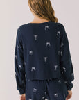 Back view of woman wearing Chaser’s navy Tossed Bows Long Sleeve with allover bow design on a white background