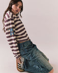Full side view of model wearingThe Rolling Stones Rugby Stones Logo Long Sleeve with red and white stripes, cropped fit, and tongue logo graphic
and jeans sitting on the floor against a plain background