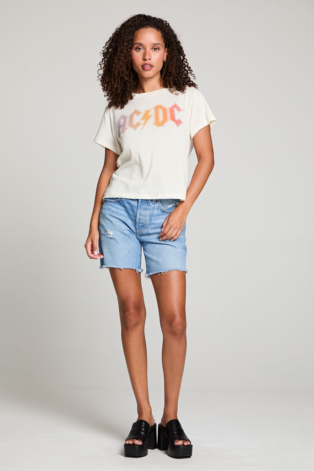 Full body view of model in AC/DC 1979 Tour Gradient Tee styled with denim shorts for a retro festival look against a plain background