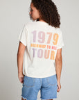 Back view of model in AC/DC 1979 Tour Gradient Tee styled with denim shorts for a retro festival look against a plain background