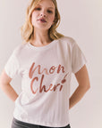 White graphic tee with Mon Cherie lettering and cherry detail over the 'i'.