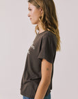 Front view of woman wearing Chaser’s brown Hot Cocoa Tee on a plain background