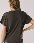 Back view of woman wearing Chaser’s brown Hot Cocoa Tee on a plain background
