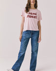 Full body view of woman wearing Chaser’s Semi Sweet Pink Tee with “semi sweet” text and blue jeans on a light background