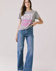 Full body view of woman wearing Chaser’s Streaky Grey Love Tee with pink text and blue jeans on a white background