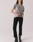 Full body view of woman wearing Chaser’s graphic Coca-Cola Highway To Anywhere Tee and black pants on a plain background