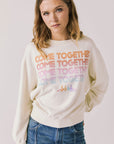 Front view of woman wearing Chaser’s The Beatles Come Together Starry White Long Sleeve with ‘COME TOGETHER’ text in rainbow colors on a plain background