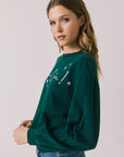 Side view of woman wearing Chaser’s green Cin Cin! Long Sleeve with “Cin Cin” text and star graphics on a plain background