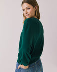 Back view of woman wearing Chaser’s green Cin Cin! Long Sleeve with “Cin Cin” text and star graphics on a plain background