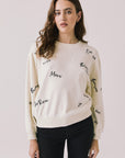 Front view of woman wearing Chaser’s Starry White French Scripts Long Sleeve with French phrases like “Merci” and “Bonjour” in black text on a white background