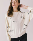Front view of woman wearing Chaser’s Starry White French Scripts Long Sleeve with French phrases like “Merci” and “Bonjour” in black text on a white background