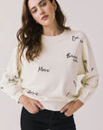Front view of woman wearing Chaser’s Starry White French Scripts Long Sleeve with French phrases like “Merci” and “Bonjour” in black text on a white background