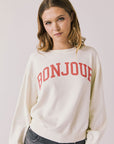 Front view of woman wearing Chaser’s starry white Bonjour Long Sleeve with ‘Bonjour’ in red text on a plain background.