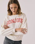 Front view of woman wearing Chaser’s starry white Bonjour Long Sleeve with ‘Bonjour’ in red text on a plain background.