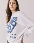 Side view of woman wearing Chaser’s light grey USA Sports Club Long Sleeve with blue USA 1969 print on a white background