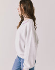 Side view of woman wearing Chaser’s Star Chainstitch Light Grey Long Sleeve on a plain background