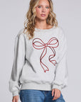 Model wearing Chaser's Merry Bow Pullover in Heather Grey with oversized red bow artwork, angled view