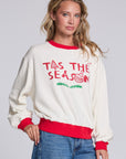 Model wearing Chaser's 'Tis the Season Pullover in Whisper White with red and green 'Tis the Season lettering and red trim, angled view