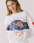 Front view of woman wearing Chaser’s white Coca-Cola Winter Sports Long Sleeve with vintage-inspired graphic design and blue jeans on a plain background