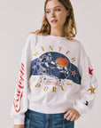 Front view of woman wearing Chaser’s white Coca-Cola Winter Sports Long Sleeve with vintage-inspired graphic design and blue jeans on a plain background