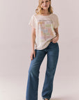 Full body view of model wearing The Beatles Ticket Stub Collage Tee in Starry White with vintage ticket graphic and classic band logo and blue jeans standing against a plain background