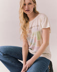 Full body view of model wearing The Beatles Ticket Stub Collage Tee in Starry White with vintage ticket graphic and classic band logo and blue jeans crouched on the floor against a plain background