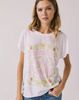 Front view of woman wearing Chaser’s The Beatles Strawberry Fields Forever White Tee with floral and pink text design on a plain background