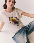Model wearing the Jackson Hole Sunset Tee in white with scenic Western graphic with graphic design and ripped jeans sitting on a plain background